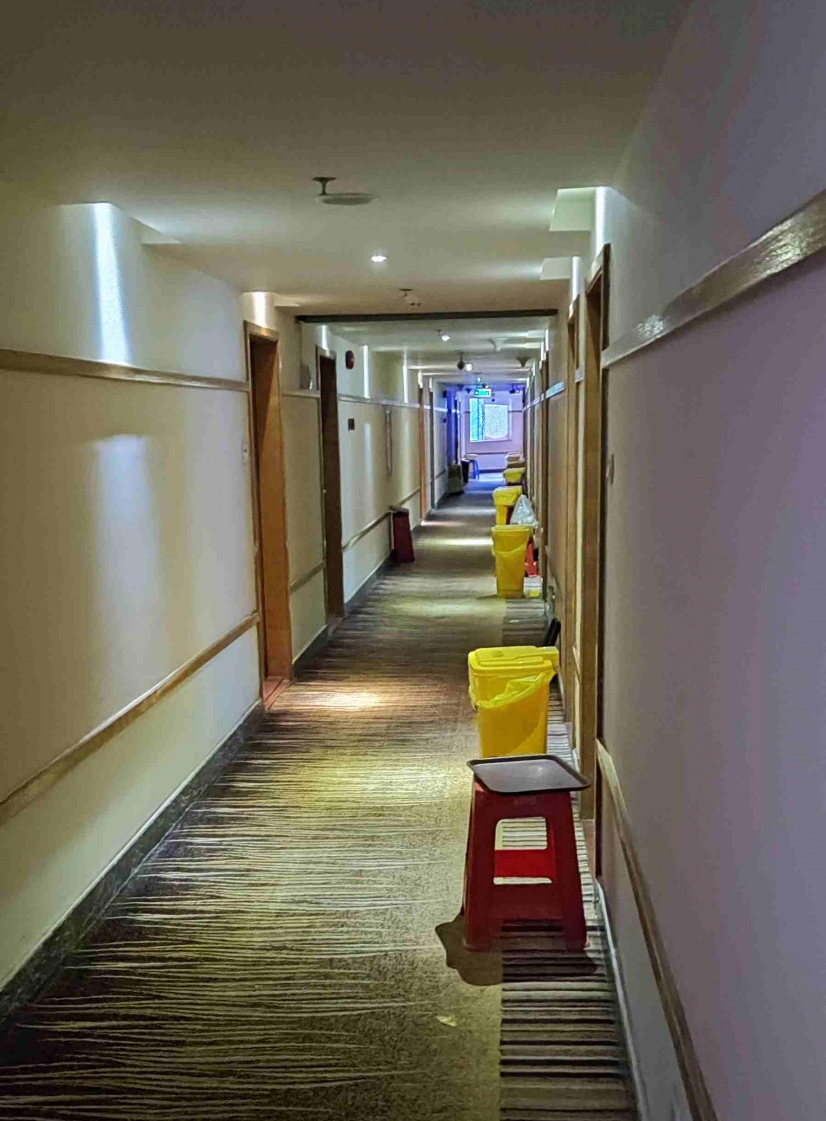 隔離酒店的走廊，房間外放置了一個黃色膠桶及褐色盤子。