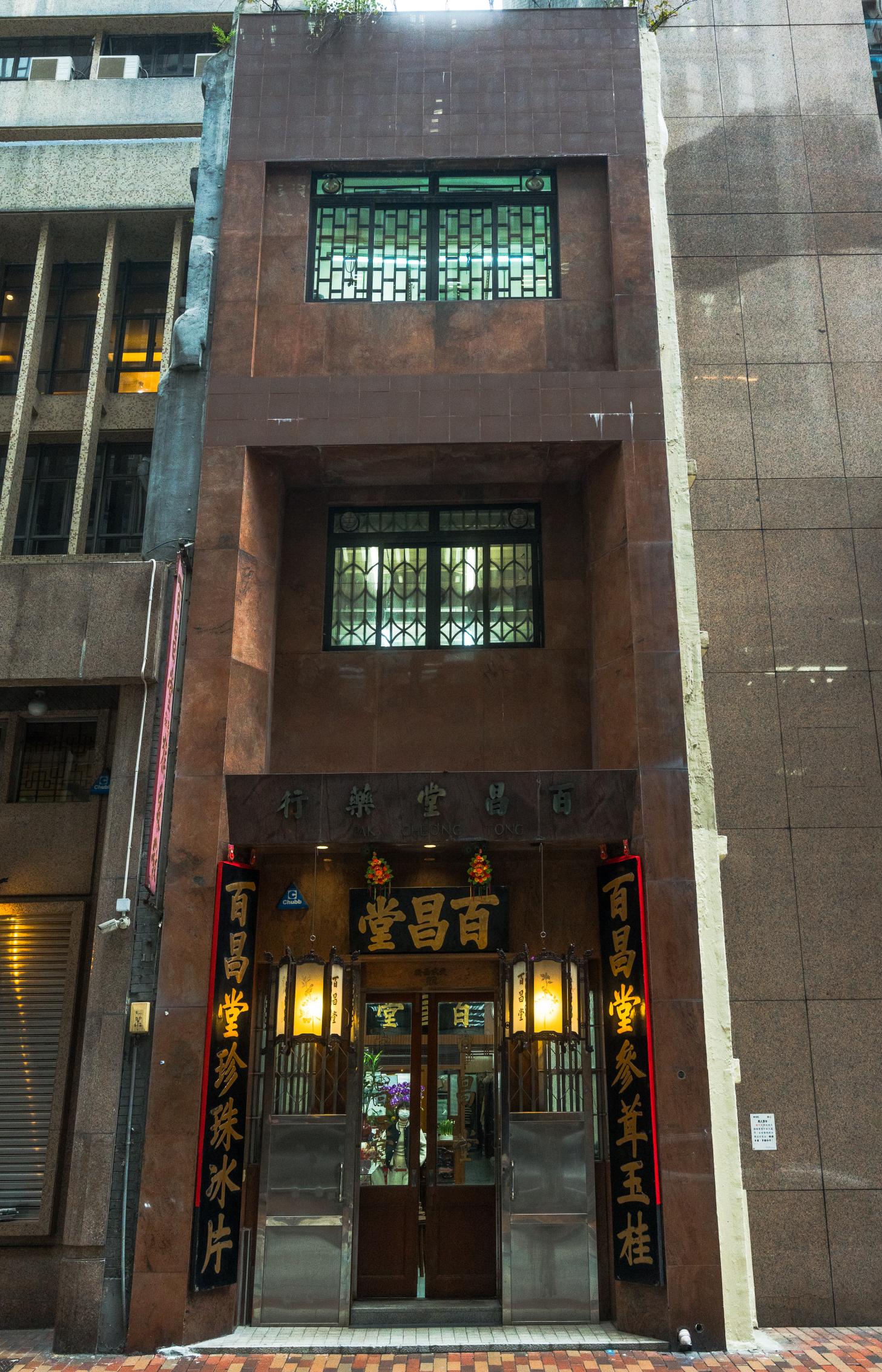 百昌堂樓高三層、混合中西風格，門口簪花掛紅黑底金漆招牌，左右相對的牌匾記錄了百昌堂主要售賣的中藥材。 